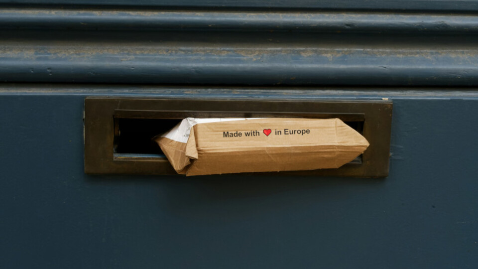 A cardbox box rammed halfway through a mailbox that is clearly too small for it. The phrase, "Made with love in Europe" is visible on the box.